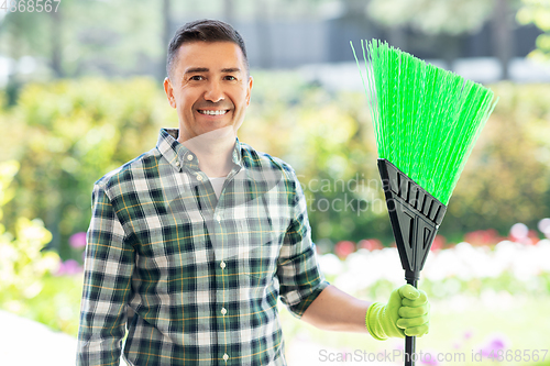 Image of happy middle-aged man with broom at garden