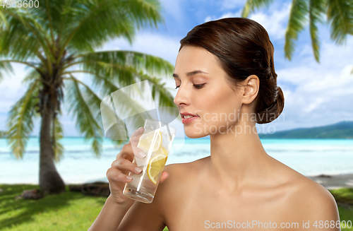 Image of woman drinking ice water with lemon over beach