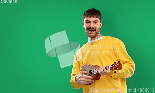 Image of happy man playing ukulele guitar over green