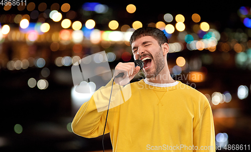 Image of man with microphone singing over night city lights