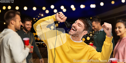 Image of man with microphone singing at night rooftop party