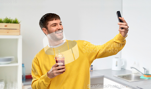 Image of happy man with smartphone and juice taking selfie