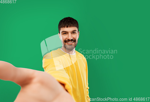 Image of happy young man in yellow sweatshirt making selfie