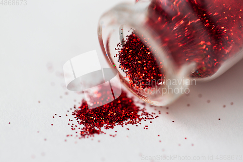 Image of red glitters poured from small glass bottle