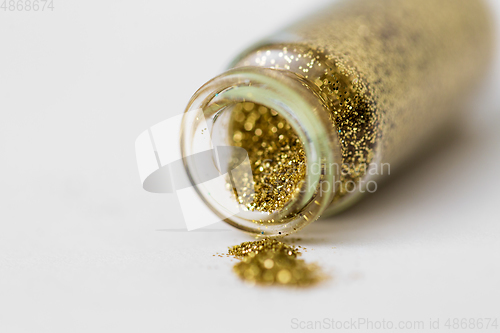 Image of golden glitters poured from small glass bottle