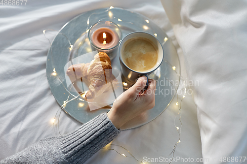 Image of hand of woman drinking coffee with croissant