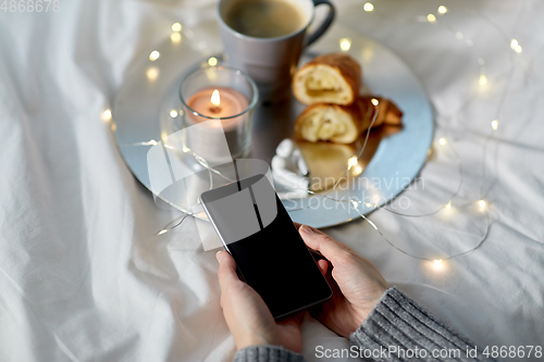 Image of hands with smartphone, croissant and coffee in bed