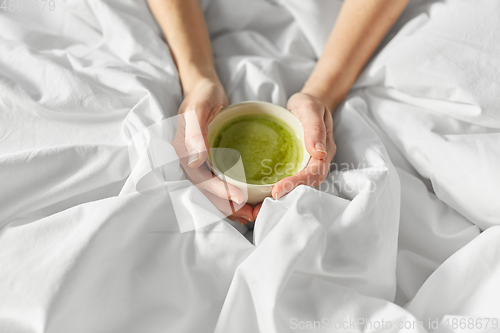 Image of hands of woman with cup of matcha tea in bed