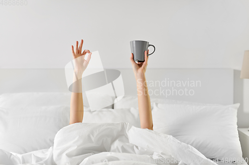 Image of woman with cup of coffee lying in bed showing ok