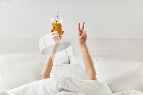 Image of hands of woman lying in bed with cup of juice