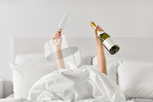 Image of hands of woman lying in bed with champagne