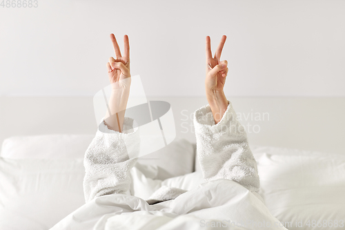 Image of hands of woman lying in bed and showing peace