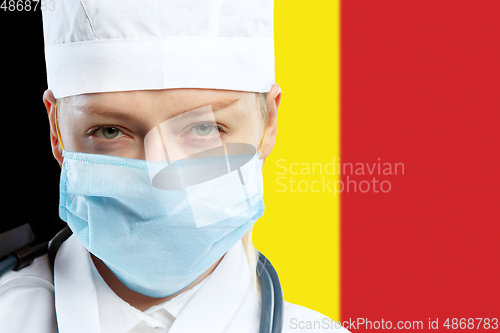 Image of Female young doctor with stethoscope and face mask praying for God with Germany national flag on background