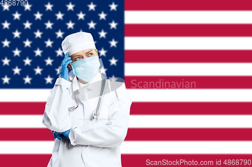 Image of Female young doctor with stethoscope and face mask praying for God with USA national flag on background