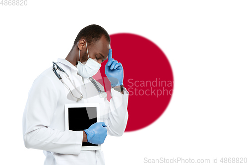 Image of Young doctor with stethoscope and face mask praying for God with Japan national flag on background