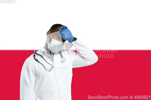 Image of Young doctor with stethoscope and face mask praying for God with Poland national flag on background