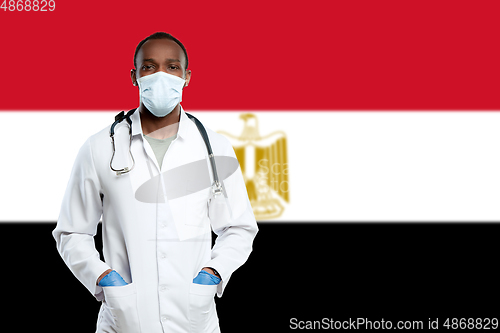 Image of Young doctor with stethoscope and face mask praying for God with Egypt national flag on background