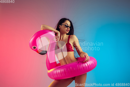 Image of Fashion portrait of young fit and sportive woman with rubber flamingo in stylish red swimwear on gradient background. Perfect body ready for summertime.