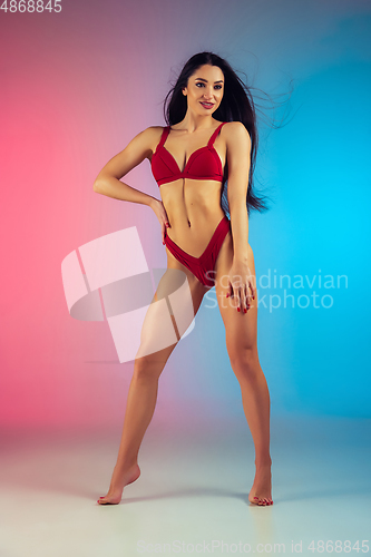 Image of Fashion portrait of young fit and sportive woman in stylish red luxury swimwear on gradient background. Perfect body ready for summertime.