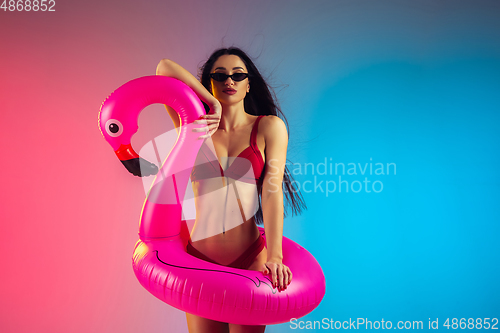 Image of Fashion portrait of young fit and sportive woman with rubber flamingo in stylish red swimwear on gradient background. Perfect body ready for summertime.