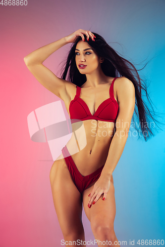 Image of Fashion portrait of young fit and sportive woman in stylish red luxury swimwear on gradient background. Perfect body ready for summertime.