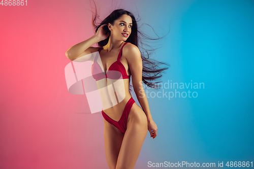 Image of Fashion portrait of young fit and sportive woman in stylish red luxury swimwear on gradient background. Perfect body ready for summertime.