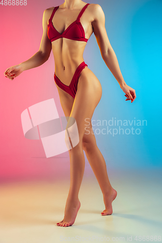 Image of Close up of young fit and sportive woman in stylish red swimwear on gradient background. Perfect body ready for summertime.