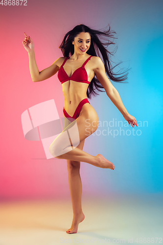 Image of Fashion portrait of young fit and sportive woman in stylish red luxury swimwear on gradient background. Perfect body ready for summertime.