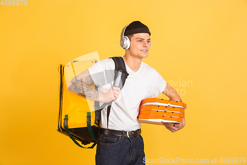 Image of Contacless delivery service during quarantine. Man delivers food and shopping bags during insulation. Emotions of deliveryman isolated on yellow background.