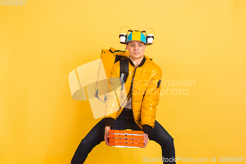 Image of Contacless delivery service during quarantine. Man delivers food and shopping bags during insulation. Emotions of deliveryman isolated on yellow background.