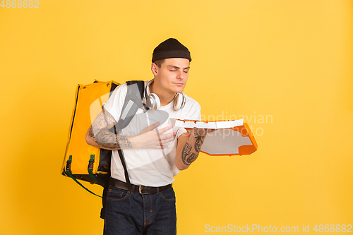 Image of Contacless delivery service during quarantine. Man delivers food and shopping bags during insulation. Emotions of deliveryman isolated on yellow background.