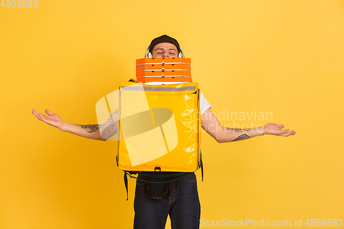 Image of Contacless delivery service during quarantine. Man delivers food and shopping bags during insulation. Emotions of deliveryman isolated on yellow background.