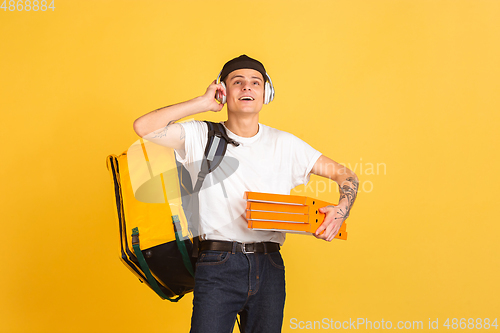 Image of Contacless delivery service during quarantine. Man delivers food and shopping bags during insulation. Emotions of deliveryman isolated on yellow background.