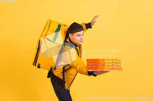 Image of Contacless delivery service during quarantine. Man delivers food and shopping bags during insulation. Emotions of deliveryman isolated on yellow background.