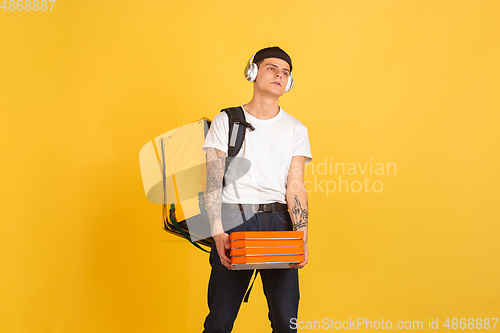 Image of Contacless delivery service during quarantine. Man delivers food and shopping bags during insulation. Emotions of deliveryman isolated on yellow background.