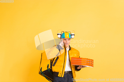 Image of Contacless delivery service during quarantine. Man delivers food and shopping bags during insulation. Emotions of deliveryman isolated on yellow background.