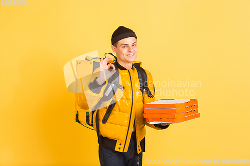 Image of Contacless delivery service during quarantine. Man delivers food and shopping bags during insulation. Emotions of deliveryman isolated on yellow background.