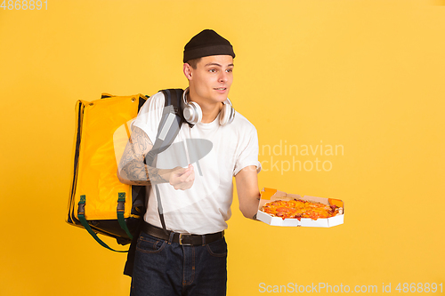 Image of Contacless delivery service during quarantine. Man delivers food and shopping bags during insulation. Emotions of deliveryman isolated on yellow background.