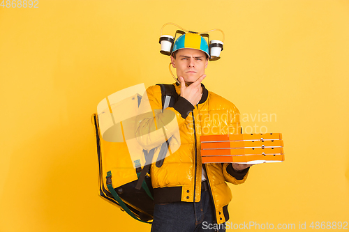 Image of Contacless delivery service during quarantine. Man delivers food and shopping bags during insulation. Emotions of deliveryman isolated on yellow background.