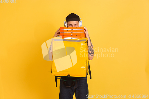 Image of Contacless delivery service during quarantine. Man delivers food and shopping bags during insulation. Emotions of deliveryman isolated on yellow background.