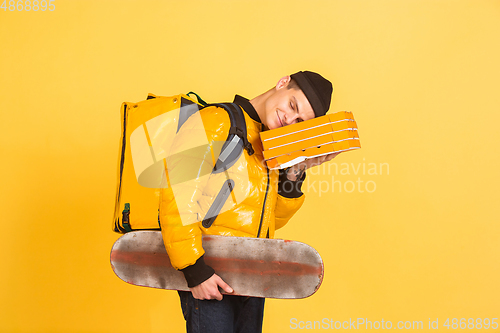 Image of Contacless delivery service during quarantine. Man delivers food and shopping bags during insulation. Emotions of deliveryman isolated on yellow background.