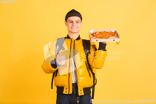 Image of Contacless delivery service during quarantine. Man delivers food and shopping bags during insulation. Emotions of deliveryman isolated on yellow background.