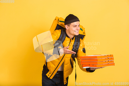 Image of Contacless delivery service during quarantine. Man delivers food and shopping bags during insulation. Emotions of deliveryman isolated on yellow background.