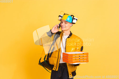 Image of Contacless delivery service during quarantine. Man delivers food and shopping bags during insulation. Emotions of deliveryman isolated on yellow background.