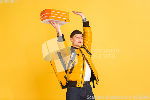 Image of Contacless delivery service during quarantine. Man delivers food and shopping bags during insulation. Emotions of deliveryman isolated on yellow background.