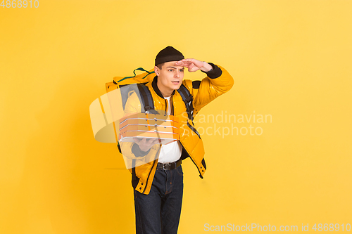 Image of Contacless delivery service during quarantine. Man delivers food and shopping bags during insulation. Emotions of deliveryman isolated on yellow background.