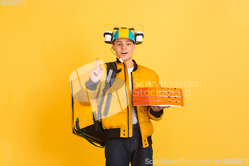 Image of Contacless delivery service during quarantine. Man delivers food and shopping bags during insulation. Emotions of deliveryman isolated on yellow background.