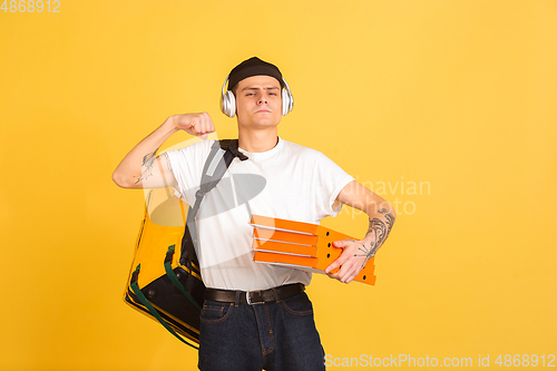 Image of Contacless delivery service during quarantine. Man delivers food and shopping bags during insulation. Emotions of deliveryman isolated on yellow background.