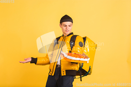 Image of Contacless delivery service during quarantine. Man delivers food and shopping bags during insulation. Emotions of deliveryman isolated on yellow background.