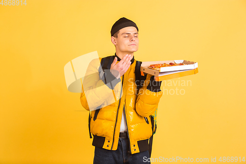 Image of Contacless delivery service during quarantine. Man delivers food and shopping bags during insulation. Emotions of deliveryman isolated on yellow background.
